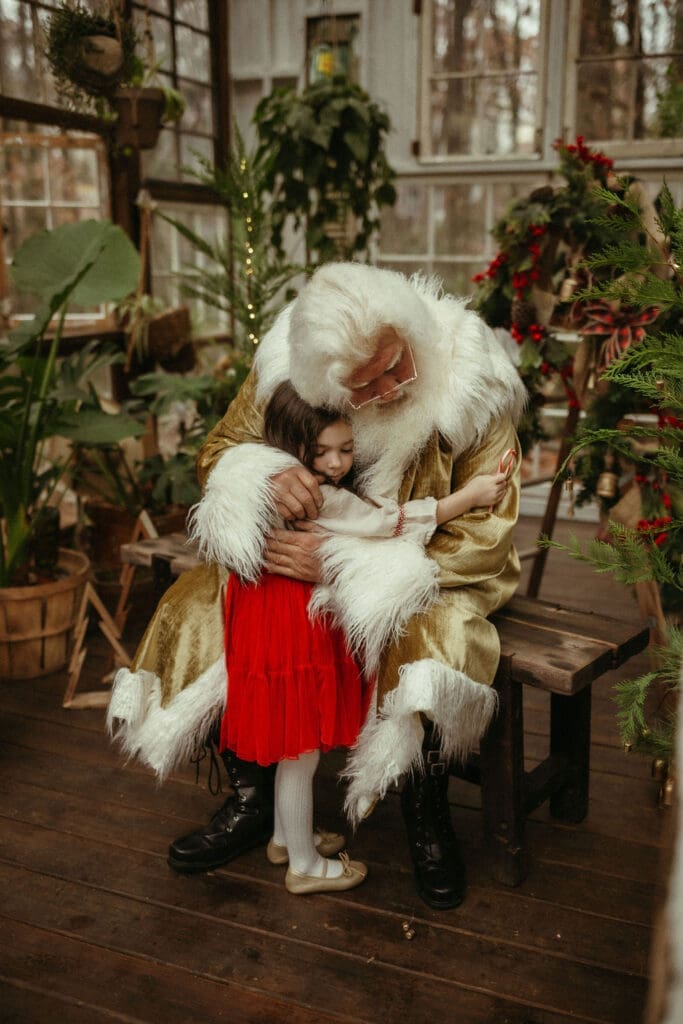 A little girl in a bright red skirt and gold ballet slippers hugging hippie Santa at Das Hinterhaus in Marietta, GA. 