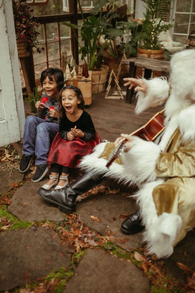 Two kids make surprised faces while sitting with hippie Santa at Das Hinterhaus. 