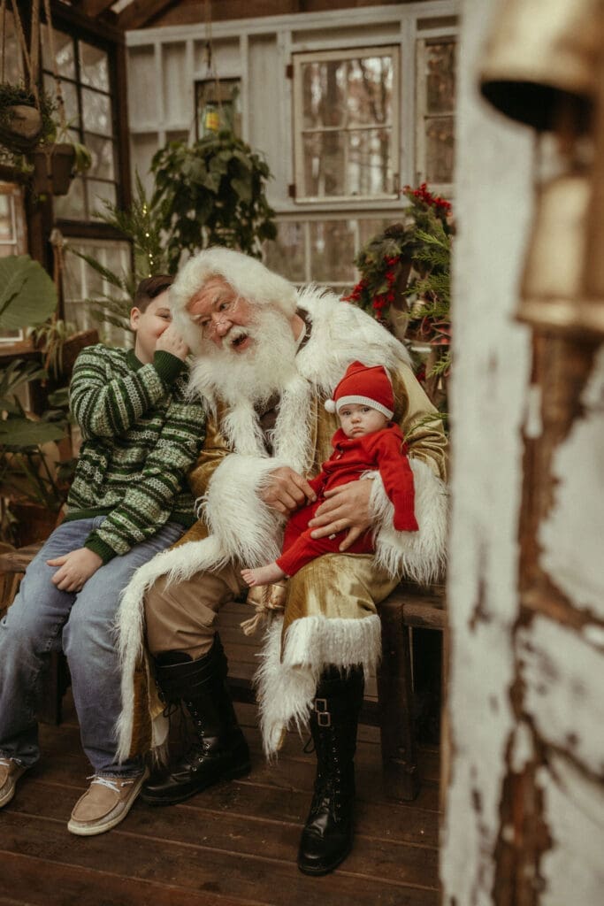 A boy whispers his Christmas wish to Santa who is holding his baby brother. 