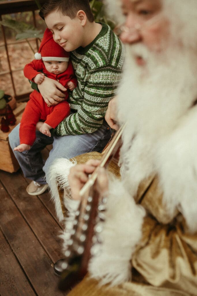 A boy holds his baby brother while The Singing Santa of Atlanta plays them a song at Das Hinterhaus studio.