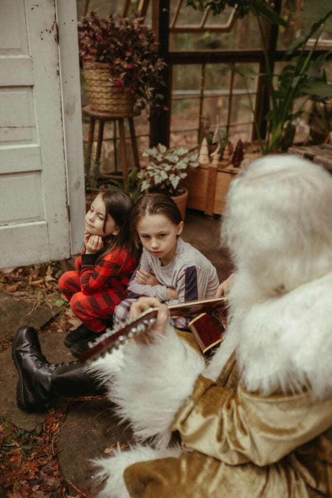 Two girls sitting with The Singing Santa of Atlanta who is playing them a song on his guitar at Das Hinterhaus studio.
