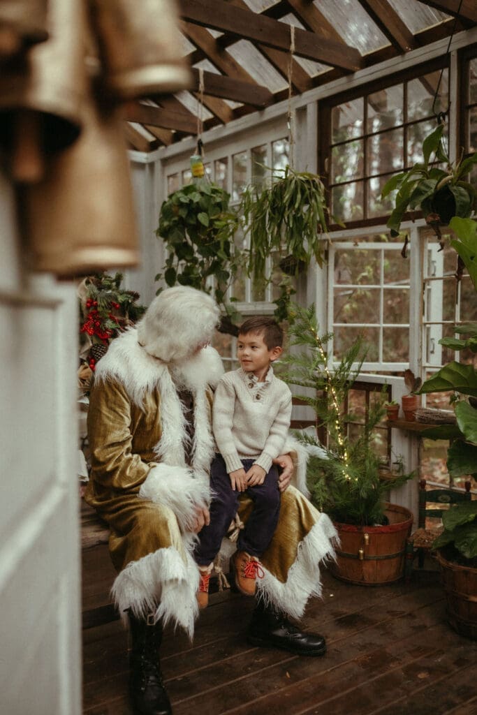 A young boy in a white sweater sitting in groovy Santa's lap at Das Hinterhaus Studio. 