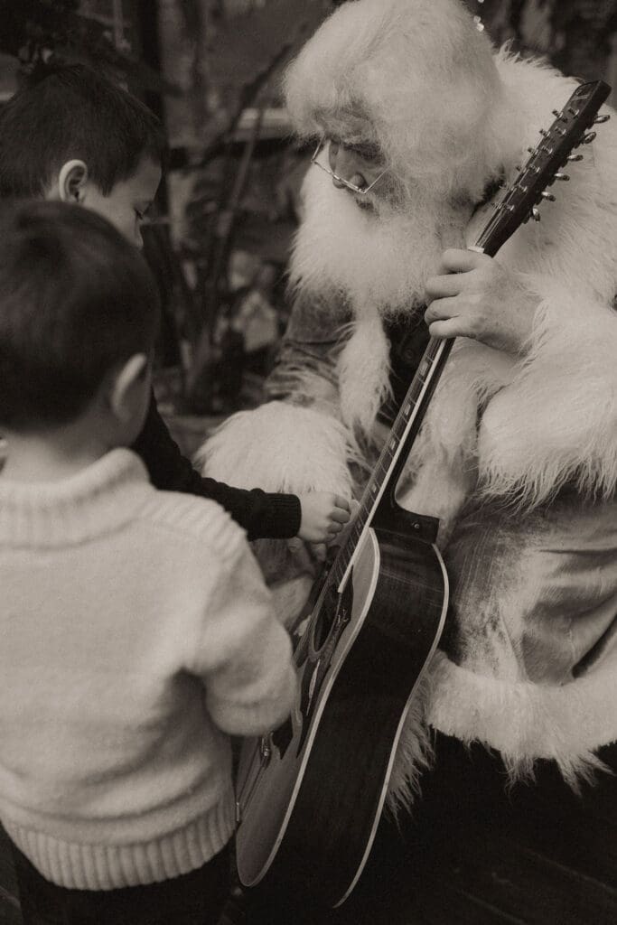 The singing Santa of Atlanta showing two young boys his guitar. 