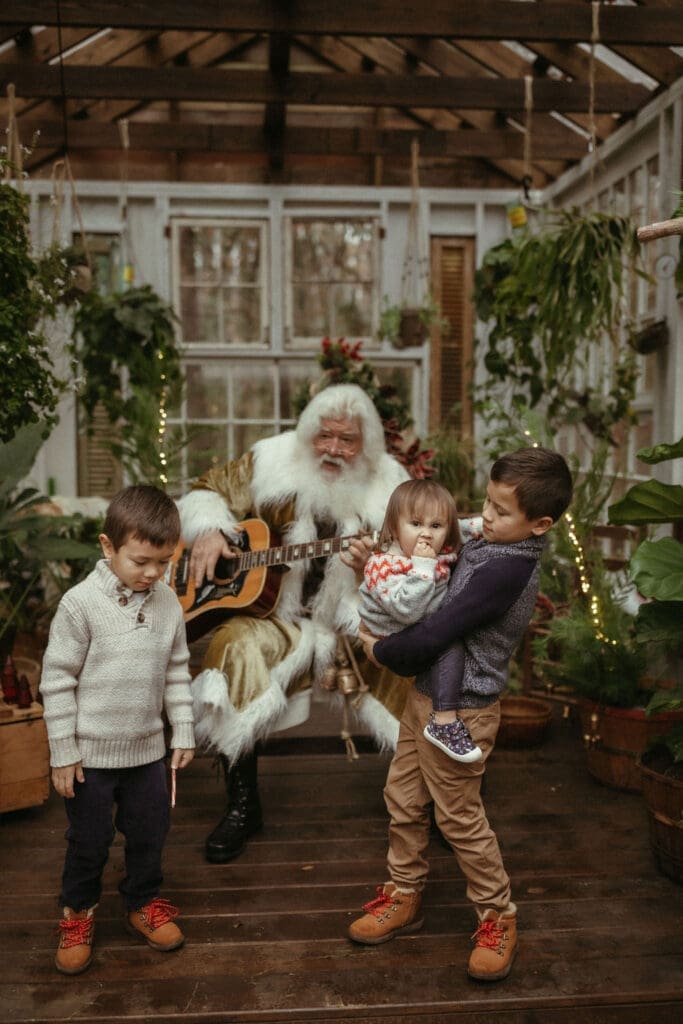 The singing Santa of Atlanta playing guitar for three kids who are dancing to the music at Das Hinterhaus. 
