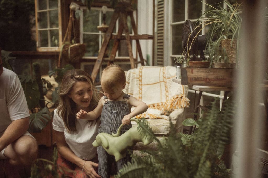 A mom sitting with her toddler as he pours water out from his cute weaner dog watering can in Das Hinterhaus greenhouse studio. 