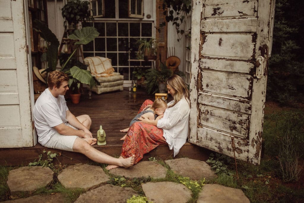 A toddler boy kissing his mom's pregnant belly while his dad watches beside them. 