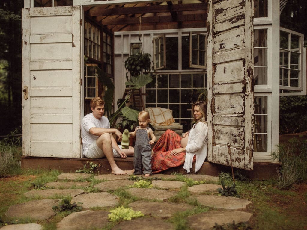 An expecting mom and dad leaning against the doorframe of Das Hinterhaus while watching their toddler play. 