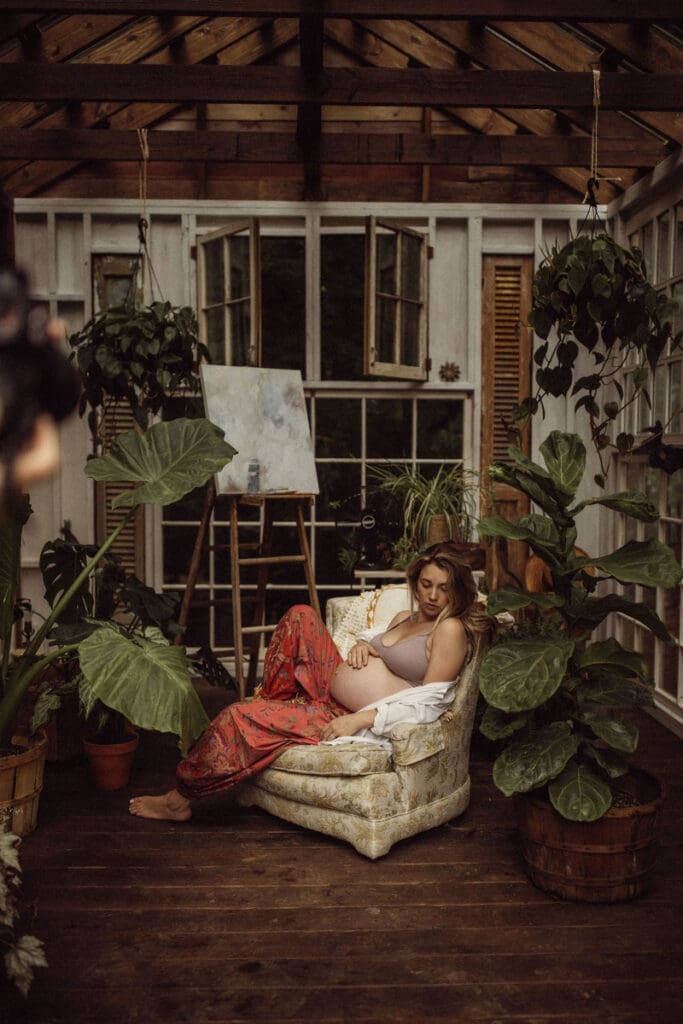 A pregnant woman in red pants and a lavender bra sitting in a chair inside Das Hinterhaus. 