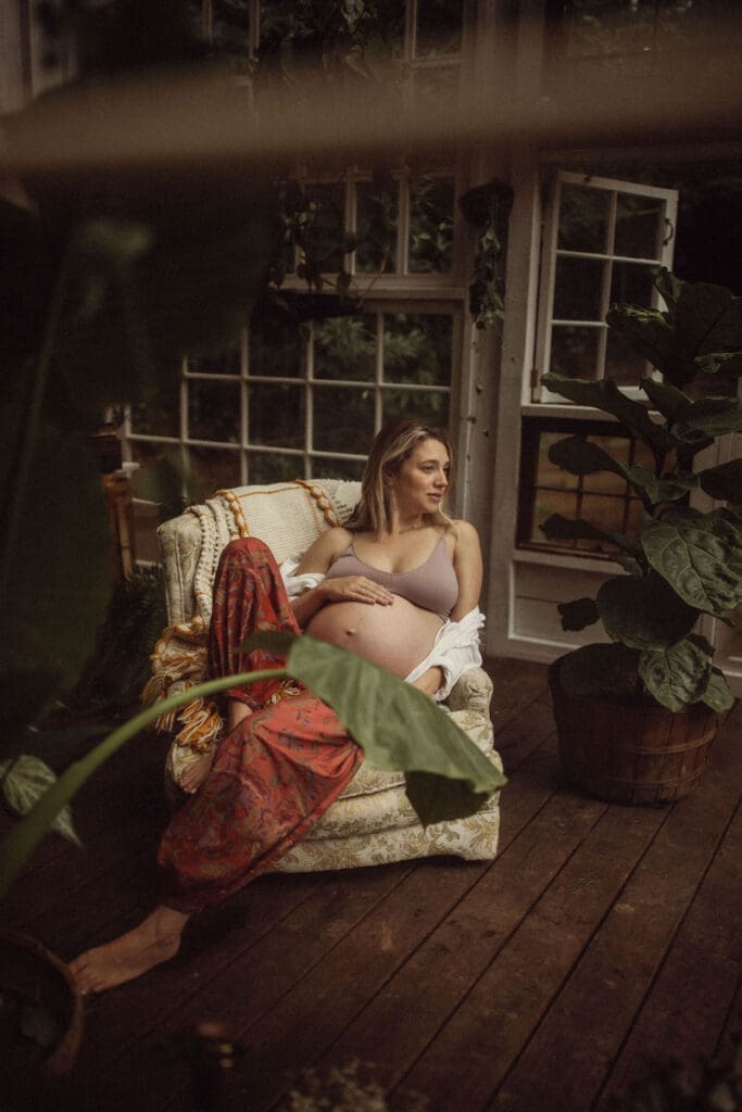A pregnant blonde woman in red pants and a lavender bra sitting in a chair inside Das Hinterhaus. 