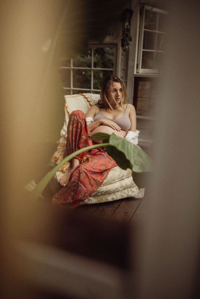 A pregnant mom in red pants and a lavender bra sitting in a chair inside Das Hinterhaus. 