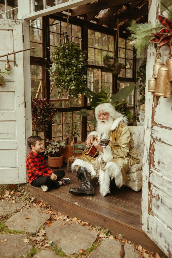 A little boy sits and listens to groovy Santa play guitar. 