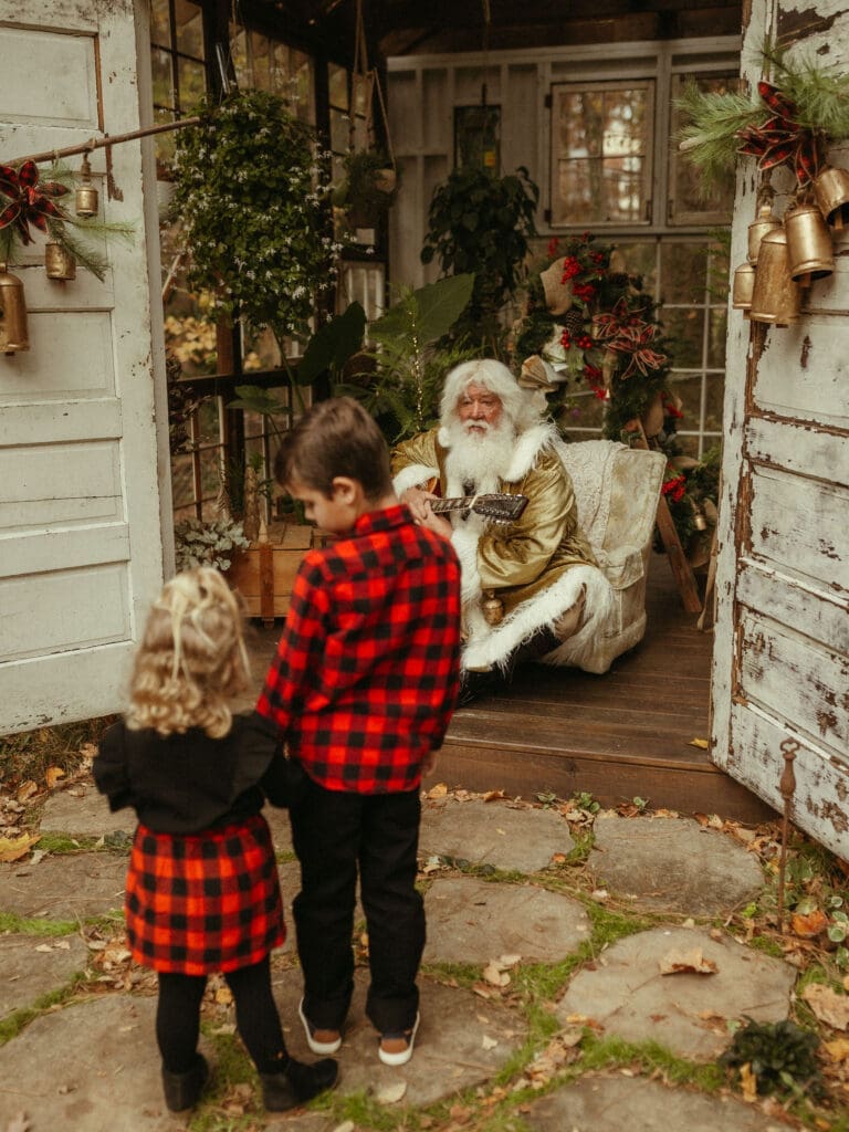 Santa playing guitar for two siblings in buffalo check outfits. 