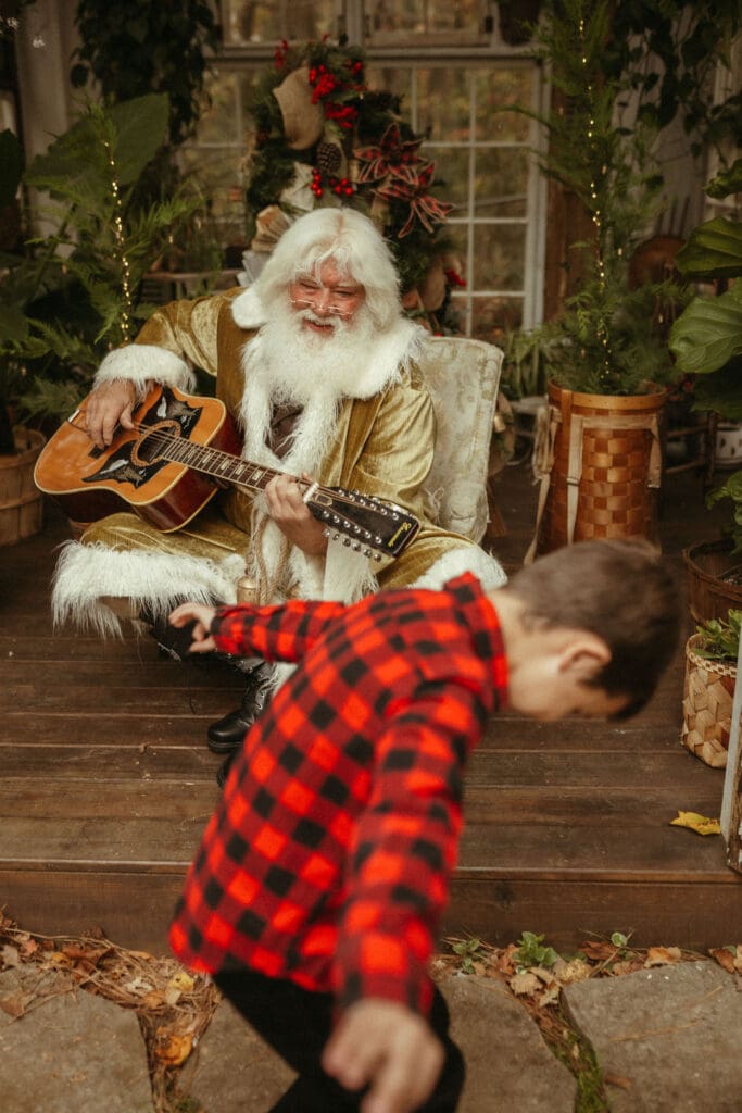 Singing Santa of Atlanta playing a song on his guitar for a dancing kid. 