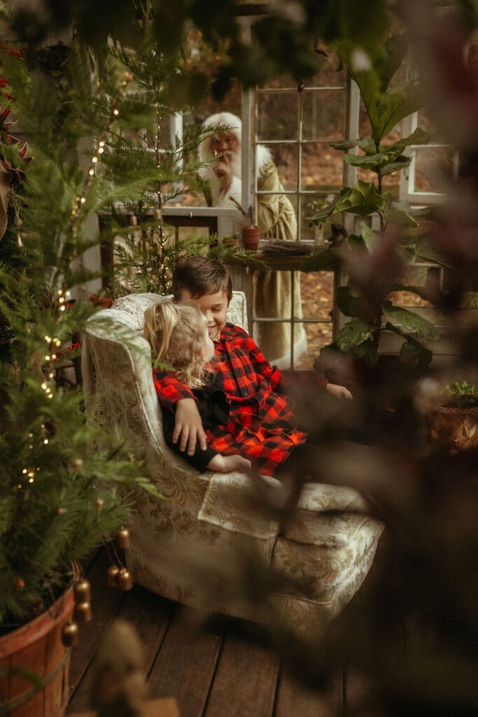 Two siblings sitting in a chair while Santa sneaks in behind them to surprise them at Das Hinterhaus. 