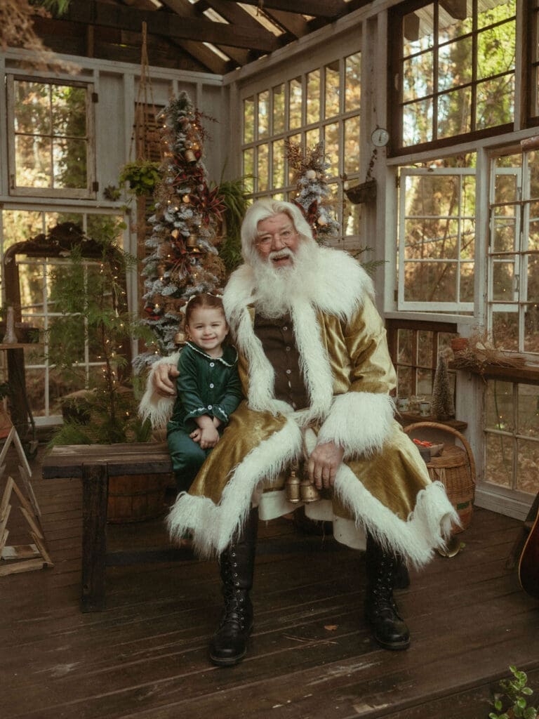 A little girl with pig tails sitting next to The Singing Santa of Atlanta at Das Hinterhaus. 