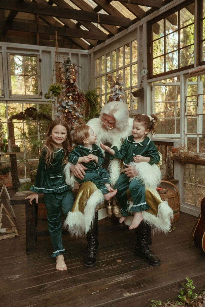 Three siblings in matching green silk pajamas sitting in Santa's lap at Das Hinterhaus. 