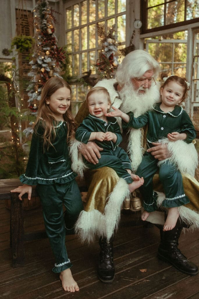 Three siblings in matching pajamas sitting in Santa's lap. 