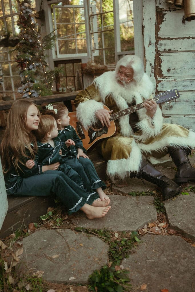 The Singing Santa of Atlanta strumming the guitar for three siblings in matching green silk pajamas. 