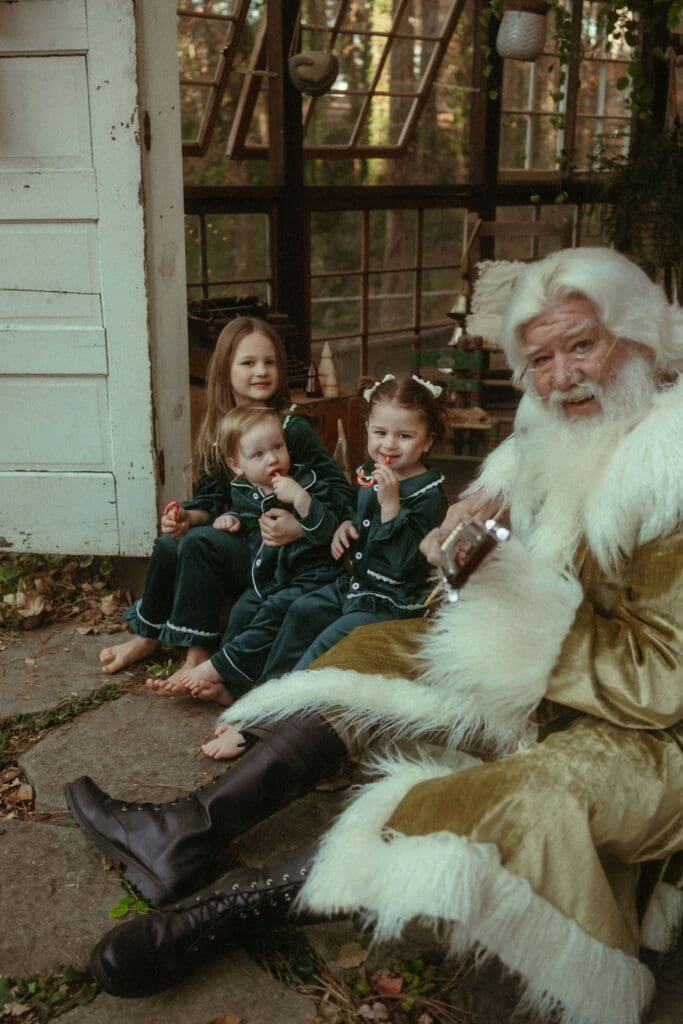 The Singing Santa of Atlanta strumming the guitar for three siblings in matching green silk pajamas at Das Hinterhaus in Marietta. 