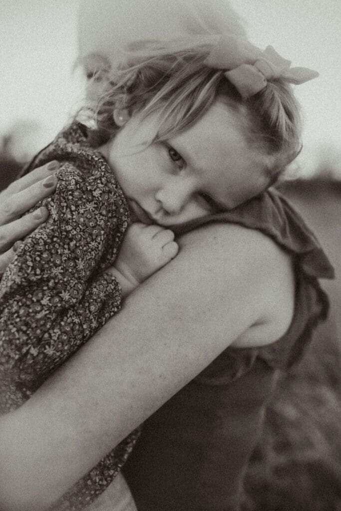 A toddler making a stink face being cuddled by her mother. 