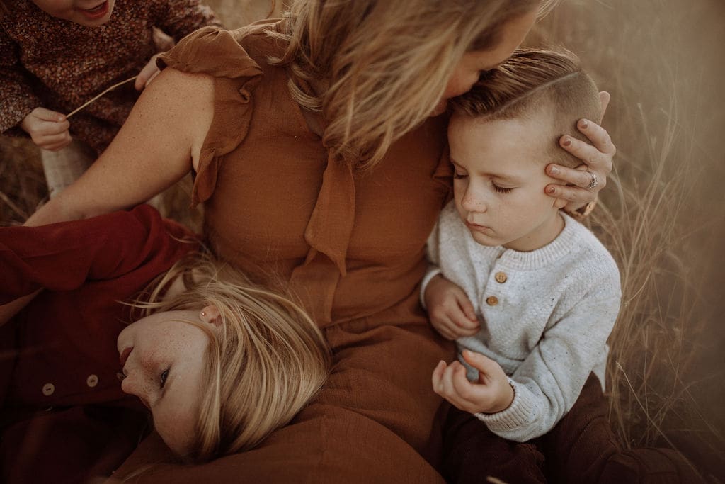 A mother leaning down to kiss her son while her daughter lays her head in her lap. 