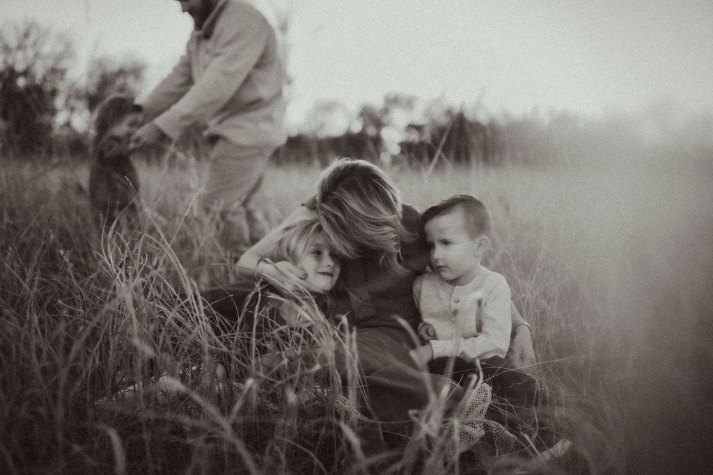 A mom holding her two oldest children while her husband dances with their toddler in the background. 
