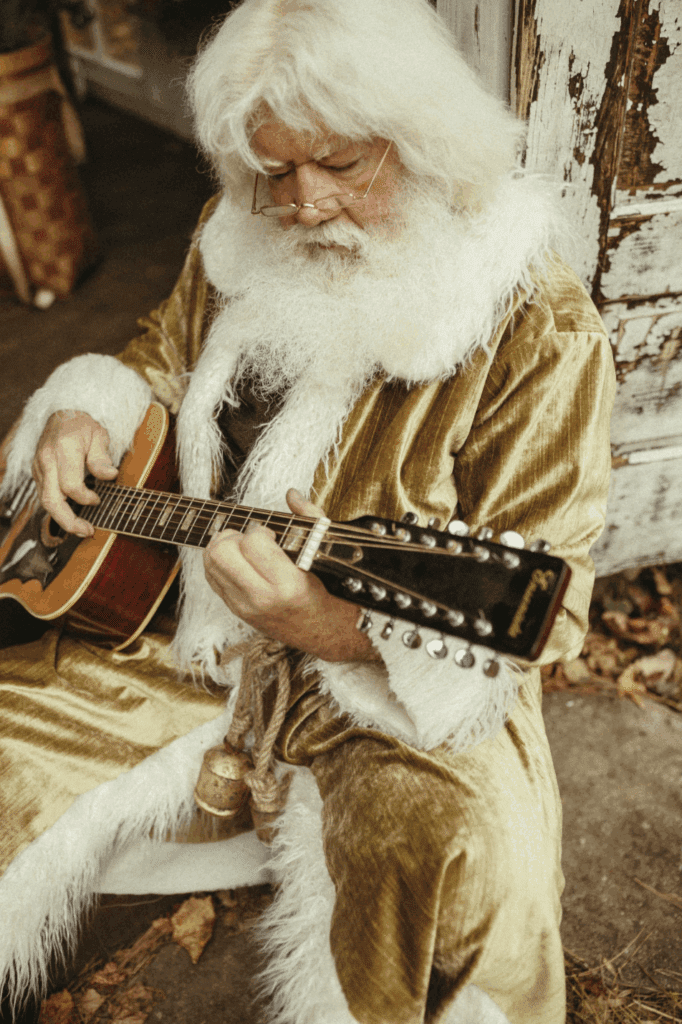 Singing Santa of Atlanta sitting in Das Hinterhaus greenhouse strumming his guitar. 