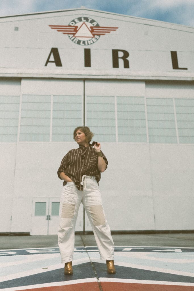 a portrait of the photographer, Melanie Dalton, in front of a Delta Air Lines hangar
