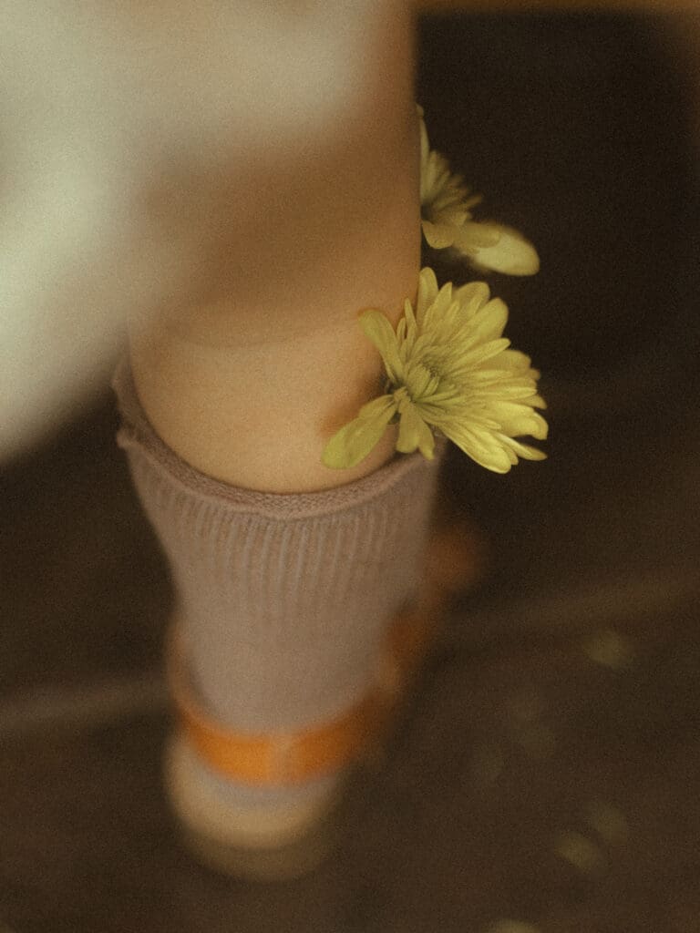 detail shot of small yellow flowers tucked into the knee high socks of a little girl wearing brown leather sandals.
