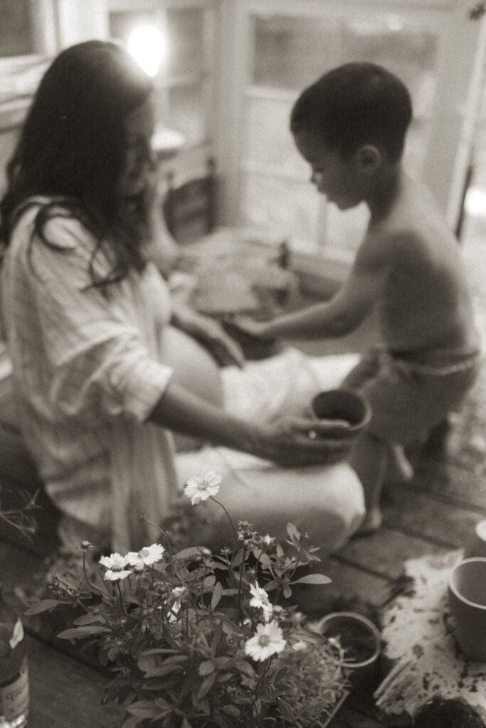 black and white shot of pregnant mom and son potting flowers in a vintage greenhouse.