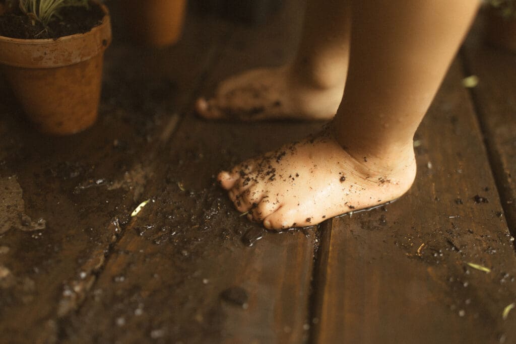 detail shot of small, bare kid feet that are wet and covered in potting soil.