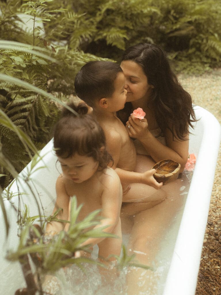 mom snuggles her two small children while sitting in a vintage tub, outside filled with water