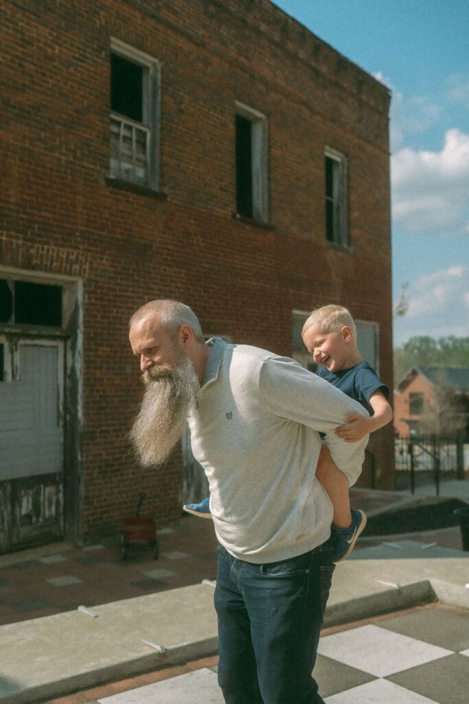 dad gives laughing toddler a piggy back ride in downtown acworth
