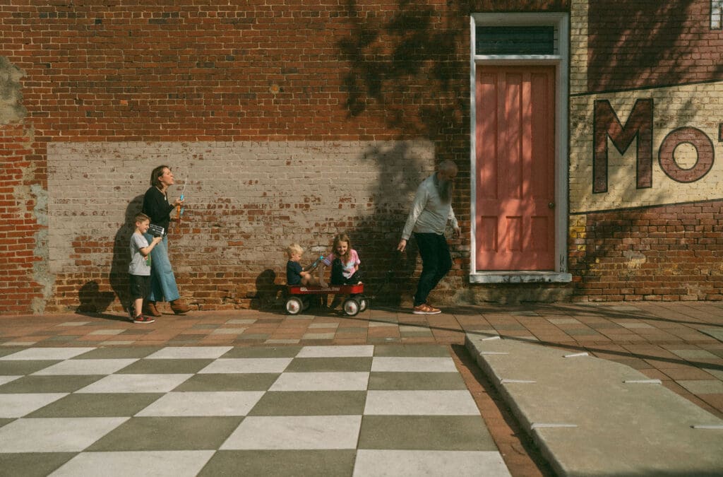 family shot in downtown acworth. dad pulls kids in wagon, mom blows bubbles and one son filmd on retro camcorder