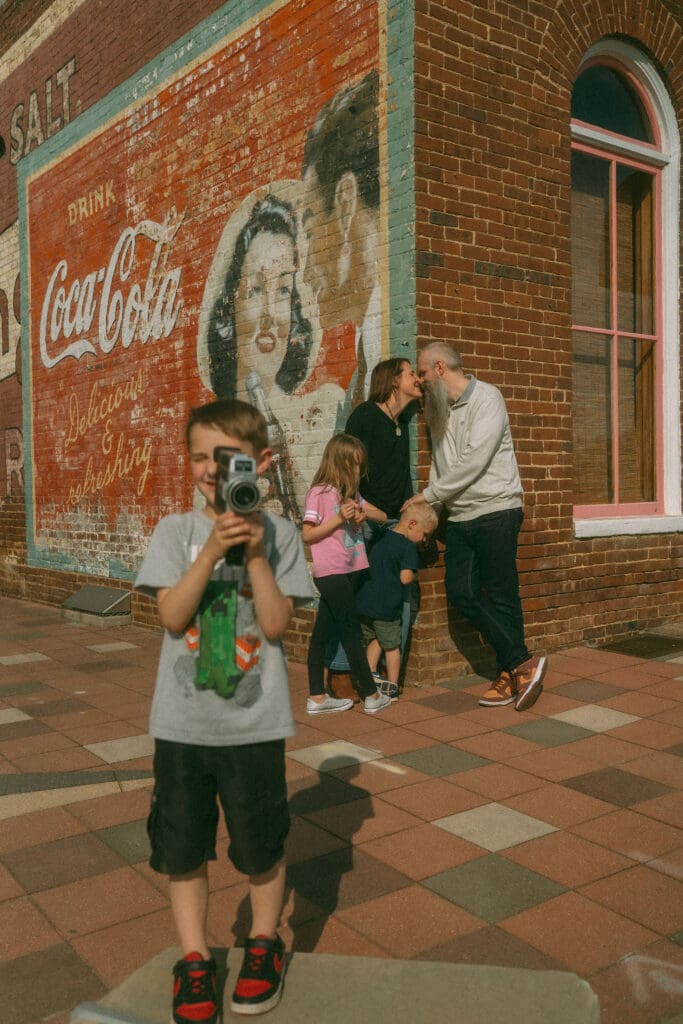 brother records photographer with camcorder while the rest of the family snuggles in the background