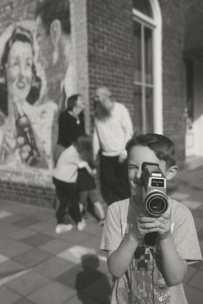 black and white close up of boy with camcorder and family in background