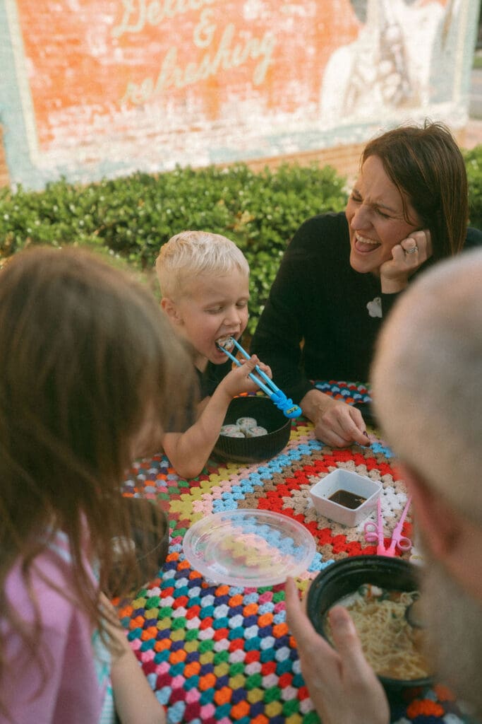 youngest son takes a big bite of sushi while mom lovingly looks on
