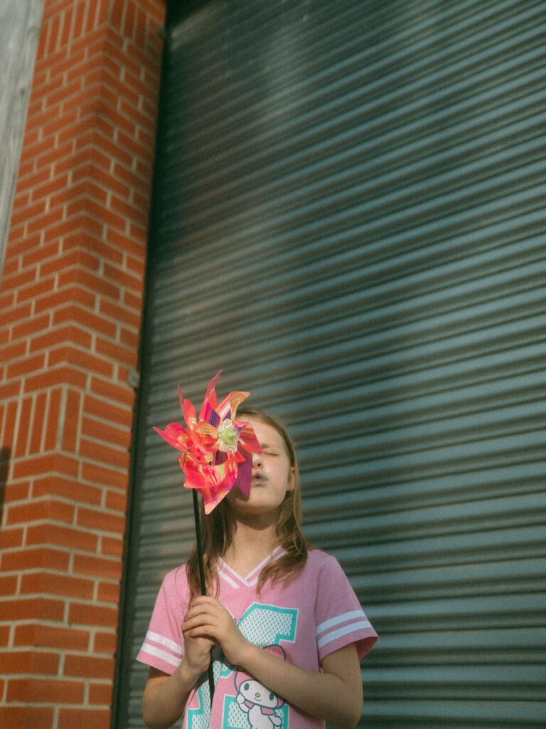 little girl blows pinwheel wile looking up into the sun