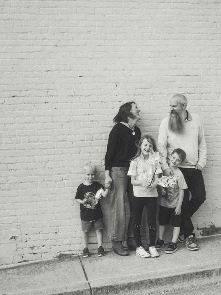 family shot against a brick wall. Mom glances at dad and laughs and kids enjoy their pinwheels