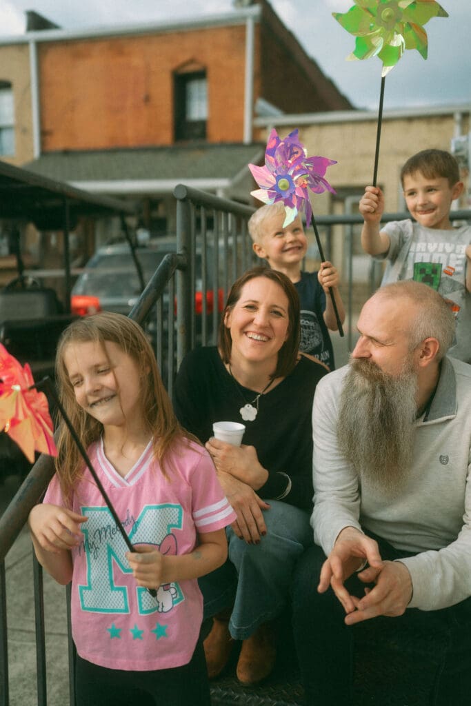 mom and dad sitting on stairs surrounded by the kids and their pinwheels